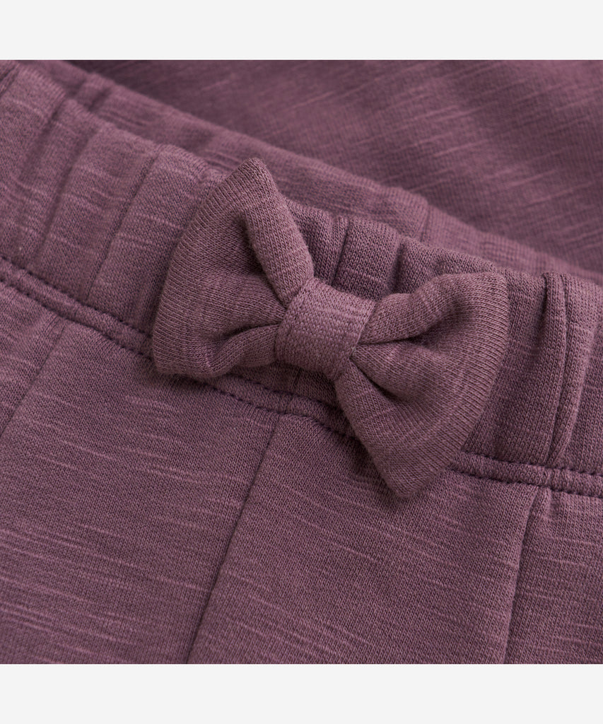 Details: These baby jogg pants are designed with comfort and style in mind. Soft and lightweight, each pair is equipped with an elastic waistband and a Bow on the front. Perfect for everyday wear.&nbsp; Color: Black plum&nbsp; Composition:&nbsp; Organic Sweat-slub Yarn 95% Cotton/ 5% Elastane &nbsp;