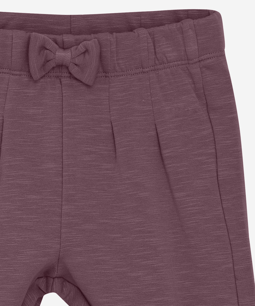 Details: These baby jogg pants are designed with comfort and style in mind. Soft and lightweight, each pair is equipped with an elastic waistband and a Bow on the front. Perfect for everyday wear.&nbsp; Color: Black plum&nbsp; Composition:&nbsp; Organic Sweat-slub Yarn 95% Cotton/ 5% Elastane &nbsp;